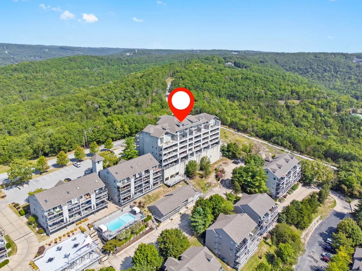 An exterior view showcasing the main building of the resort with a clear view of the swimming pool, lush greenery, and the parking area. The relaxed setting hints at a welcoming, communal environment ideal for families and groups.