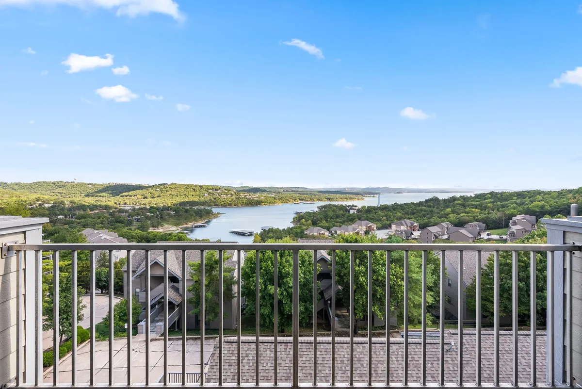 A breathtaking view of the lake, rolling hills, and sky, framed by residential buildings. The scene conveys a tranquil, scenic environment perfect for relaxation or enjoying time on a private balcony.