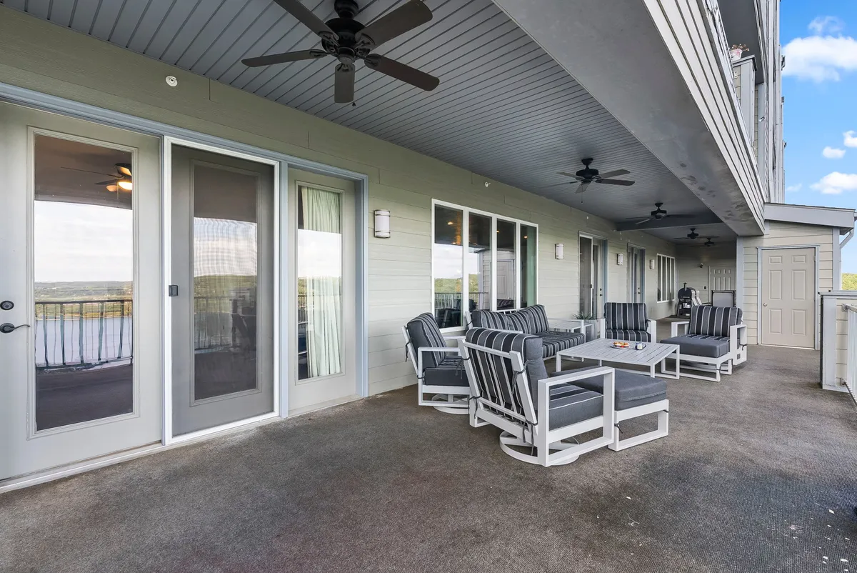 This image features a spacious outdoor seating area set on a wide deck, with sliding glass doors connecting the indoor living space to the outdoors. The deck overlooks Table Rock Lake, offering clear, expansive views of the water and sunset. Multiple seats are arranged for dining, relaxing, and socializing, highlighting the deck's capacity for gatherings and leisure activities like barbecues or sunset toasts.