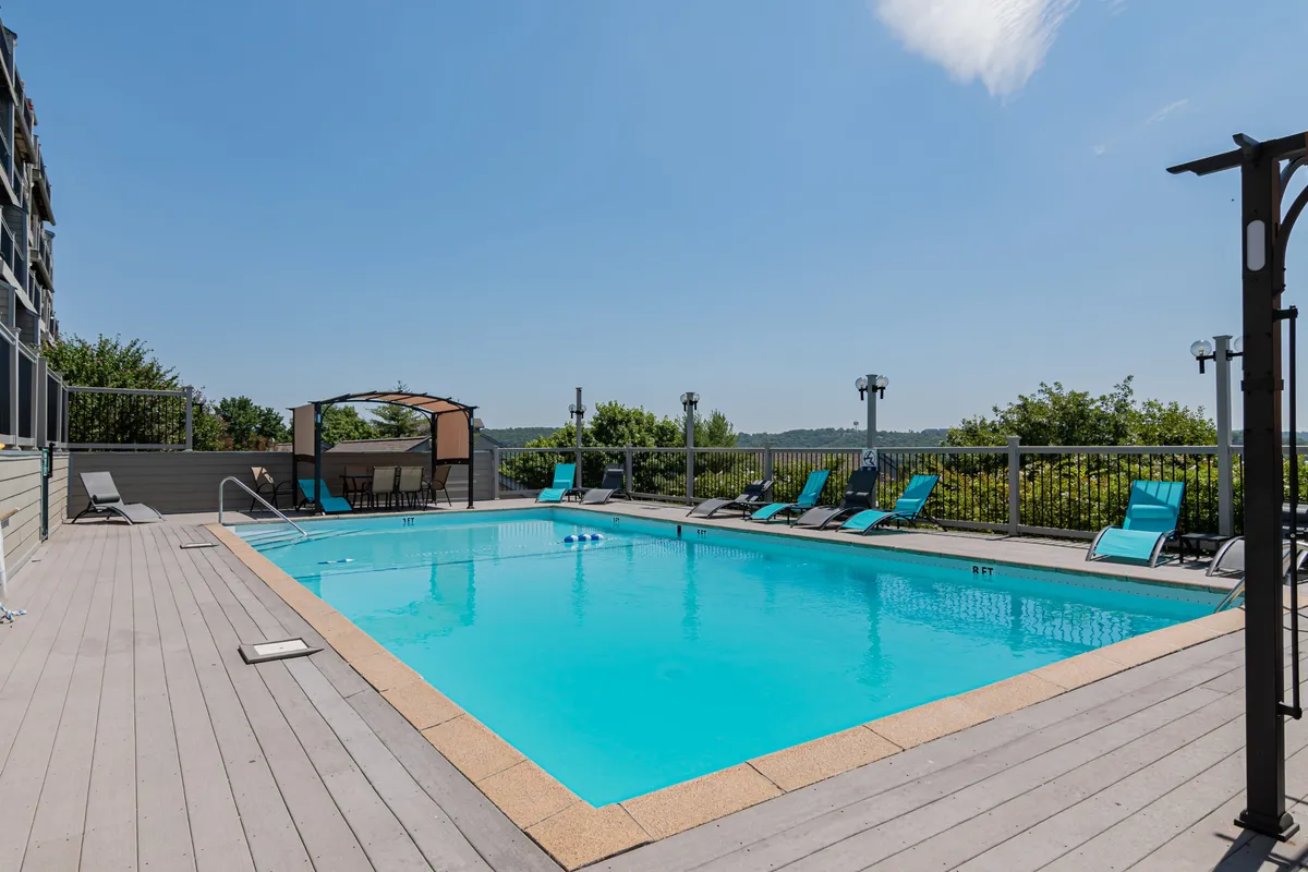 A vibrant outdoor pool area with inviting lounge chairs, a shaded canopy, and lush greenery in the background. The space is clearly designed for both relaxation and social gatherings, making it perfect for groups of all ages to enjoy time together in a resort-like atmosphere.
