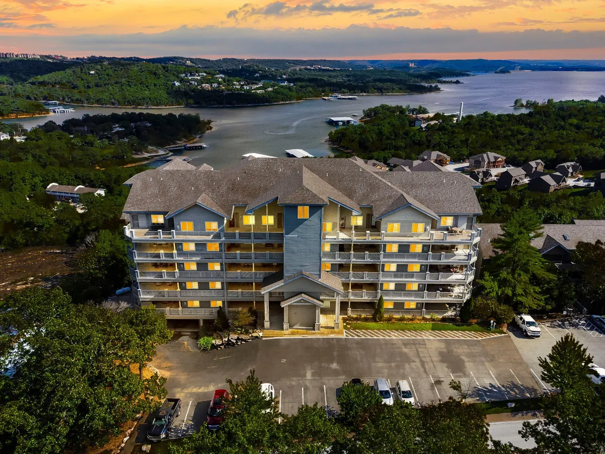 The exterior of the property with its welcoming architecture, illuminated windows, and a waterfront setting. A balcony overlooks the lake and is surrounded by a tranquil, green landscape—ideal for unwinding after a day on the water.