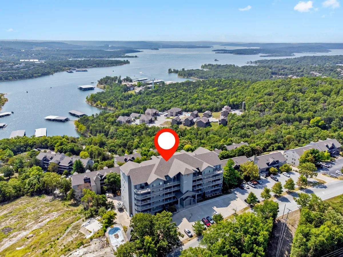 A picturesque waterfront view with lush greenery and a multi-story building, inviting guests to imagine boating, hiking, or simply relaxing while enjoying the sunset over the lake.