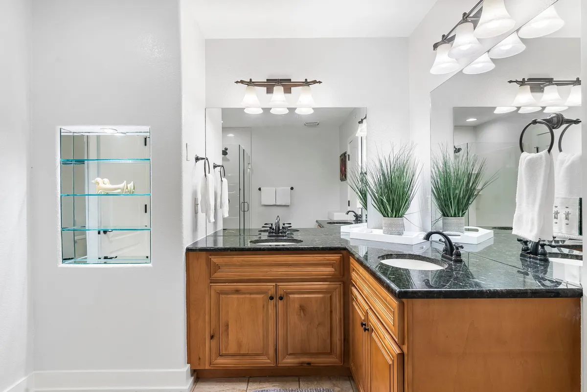 A stylish bathroom with a vanity featuring a dark countertop, open shelving with decorative items, and potted plants that add a touch of freshness. The mood is tranquil and spa-like, ideal for self-care and relaxation.