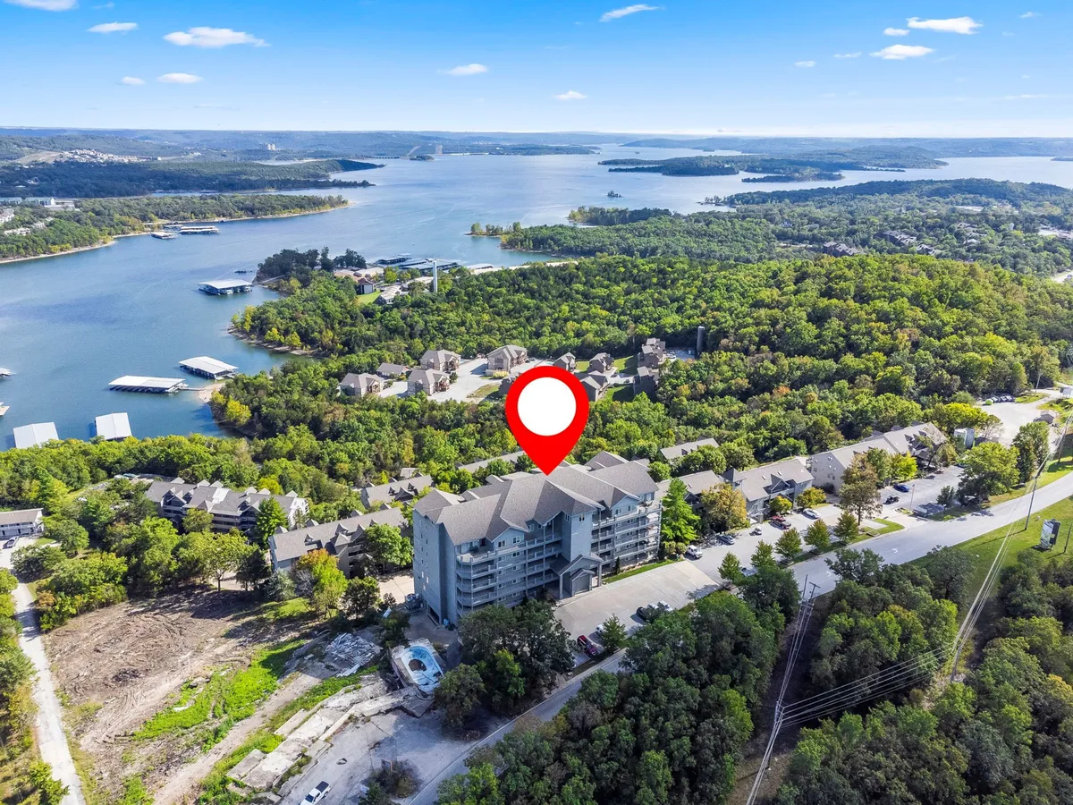 A scenic exterior perspective featuring a tranquil lake, flourishing greenery, and parts of the building structure. The setting suggests easy access to water activities and natural exploration for families and children.
