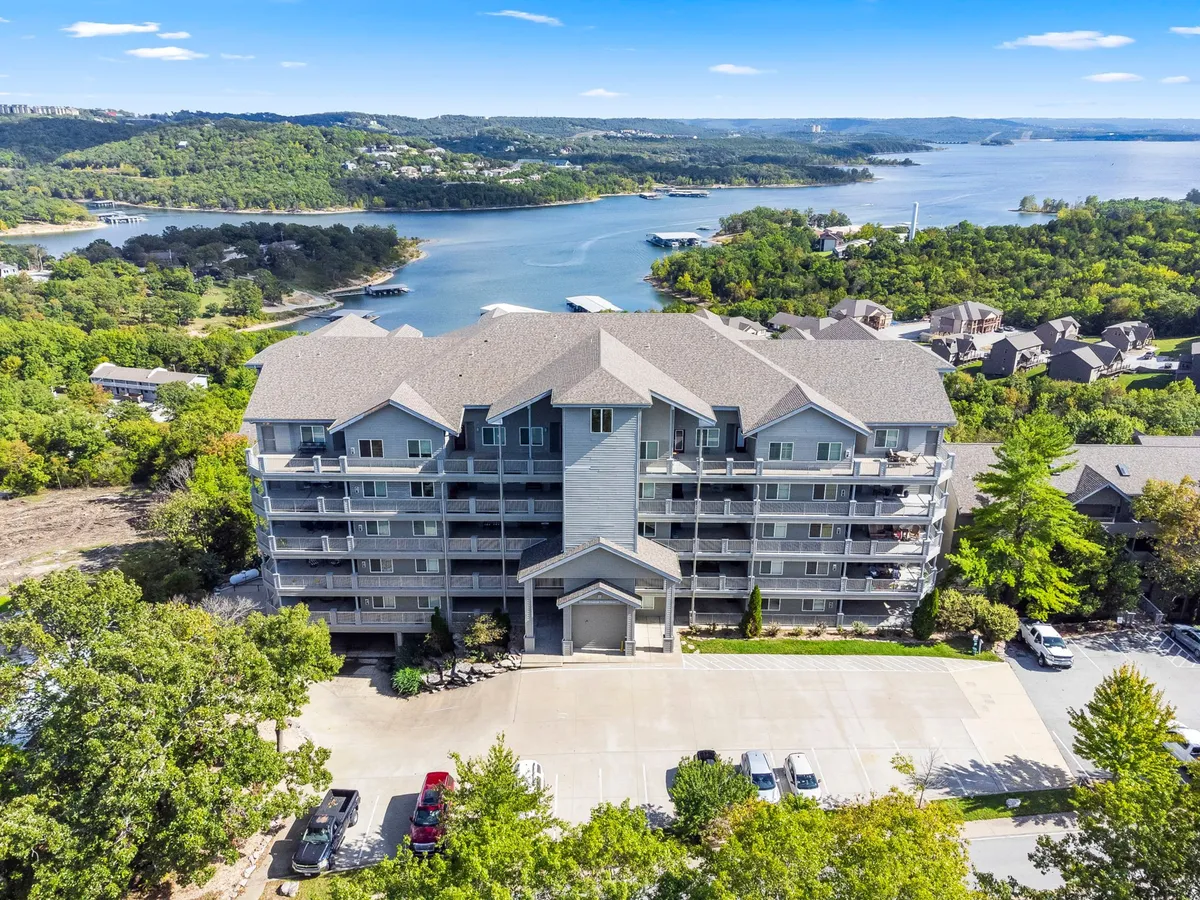 A serene exterior view of a multistory building overlooking a tranquil water body, surrounded by lush landscape. The image hints at outdoor recreation opportunities like boating and hiking while emphasizing the peaceful setting and accessibility to nature.