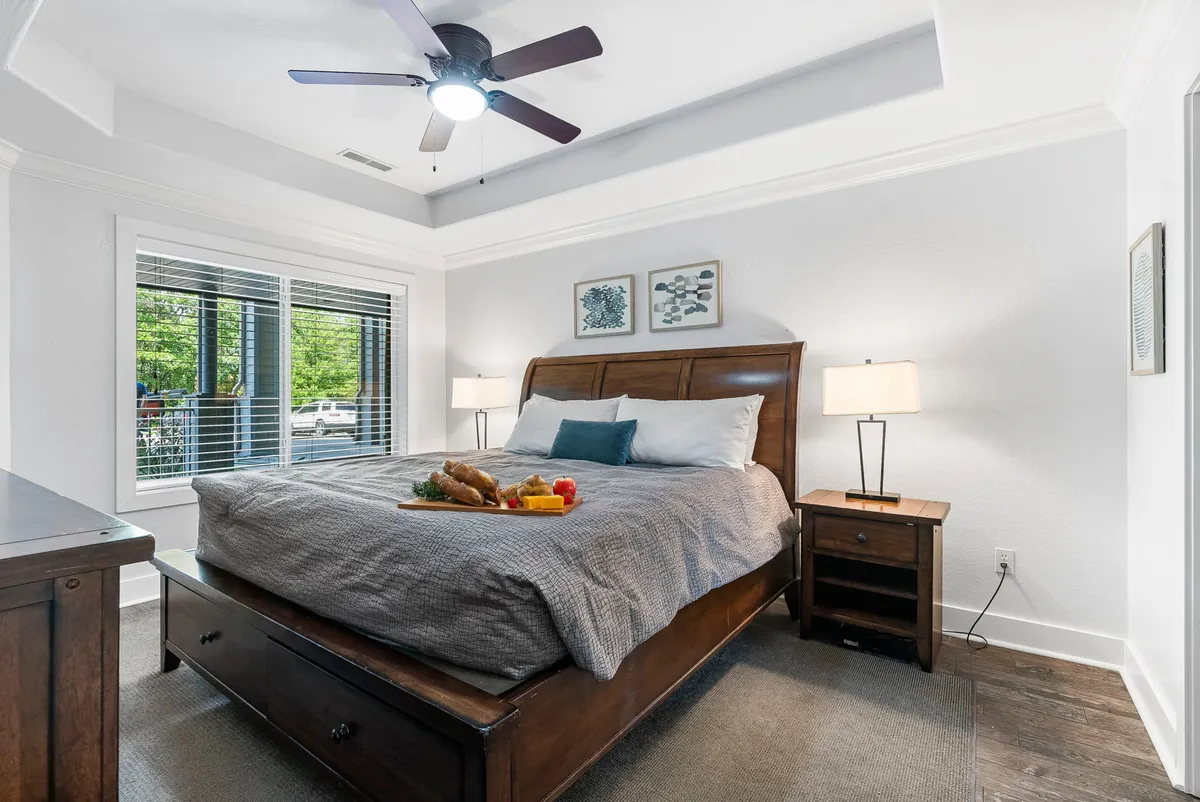 A serene bedroom with a neatly made bed adorned with plush pillows and a cozy blanket. A breakfast tray sits invitingly atop the bed, and large windows allow natural light to flood the space, giving it a bright and airy feel.
